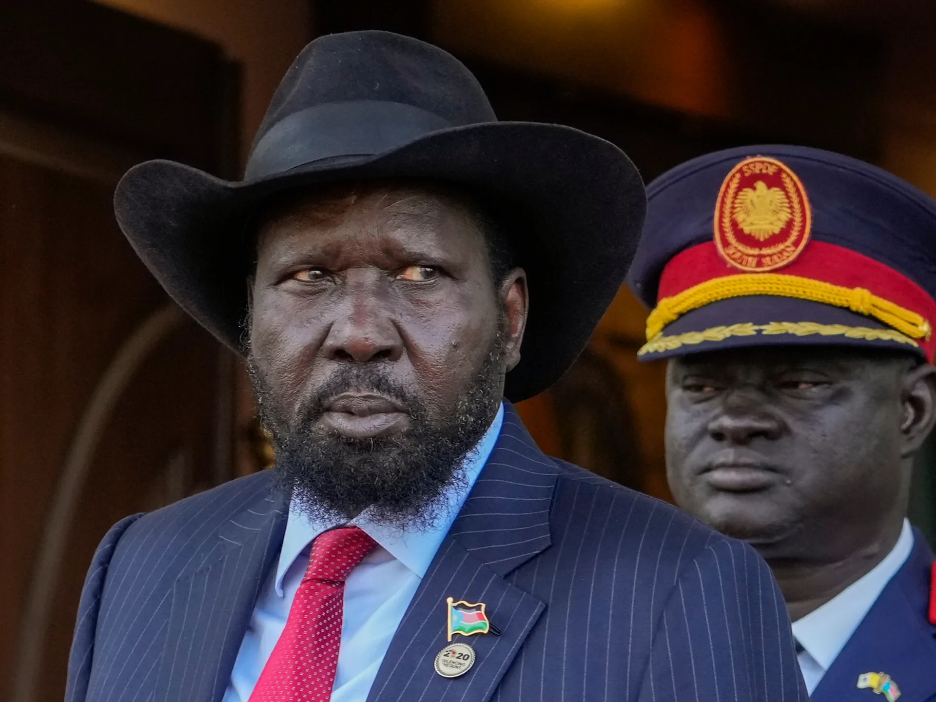 Two men in formal clothing and military-style hats pose against a dark background.
