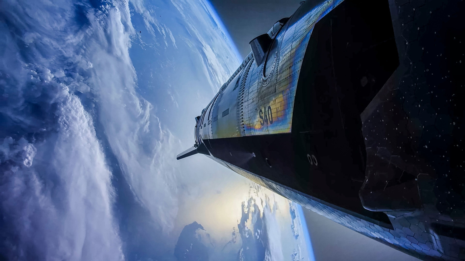 A spacecraft with dark heat-shield tiles flies above Earth's clouds and blue horizon.