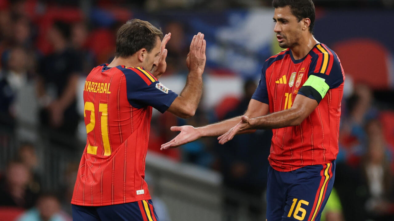 Two Spain players in red kits gesture toward each other during a match, one wearing a captain's armband.
