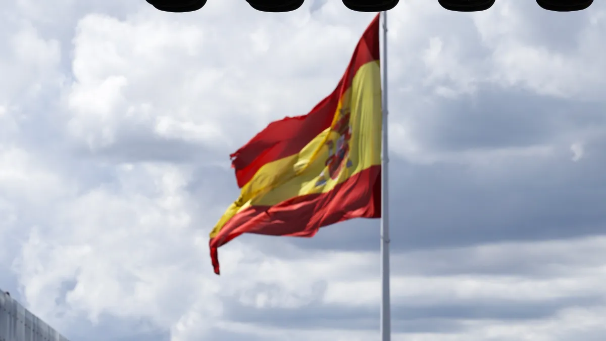 Spanish flag waving on a flagpole against a cloudy sky
