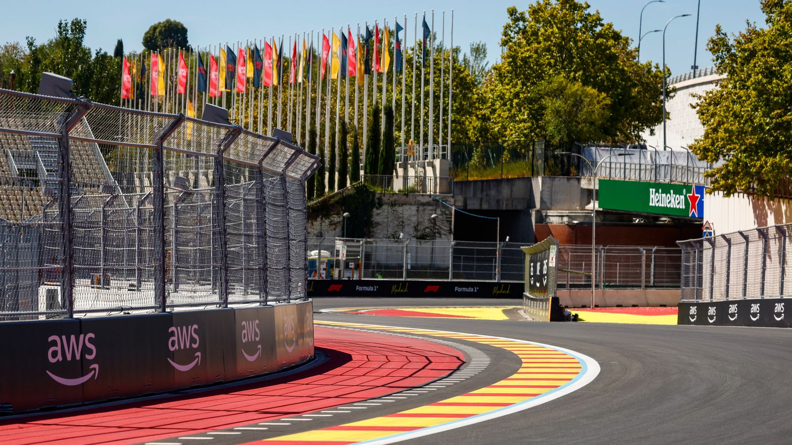 Empty Formula 1 circuit corner with colorful curbs, barriers, grandstands, flags, and advertising boards.