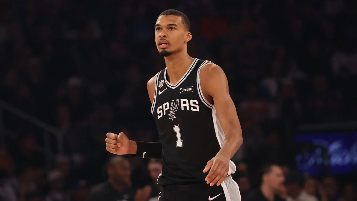 Basketball player in a black San Antonio Spurs jersey raises a clenched fist during a game.