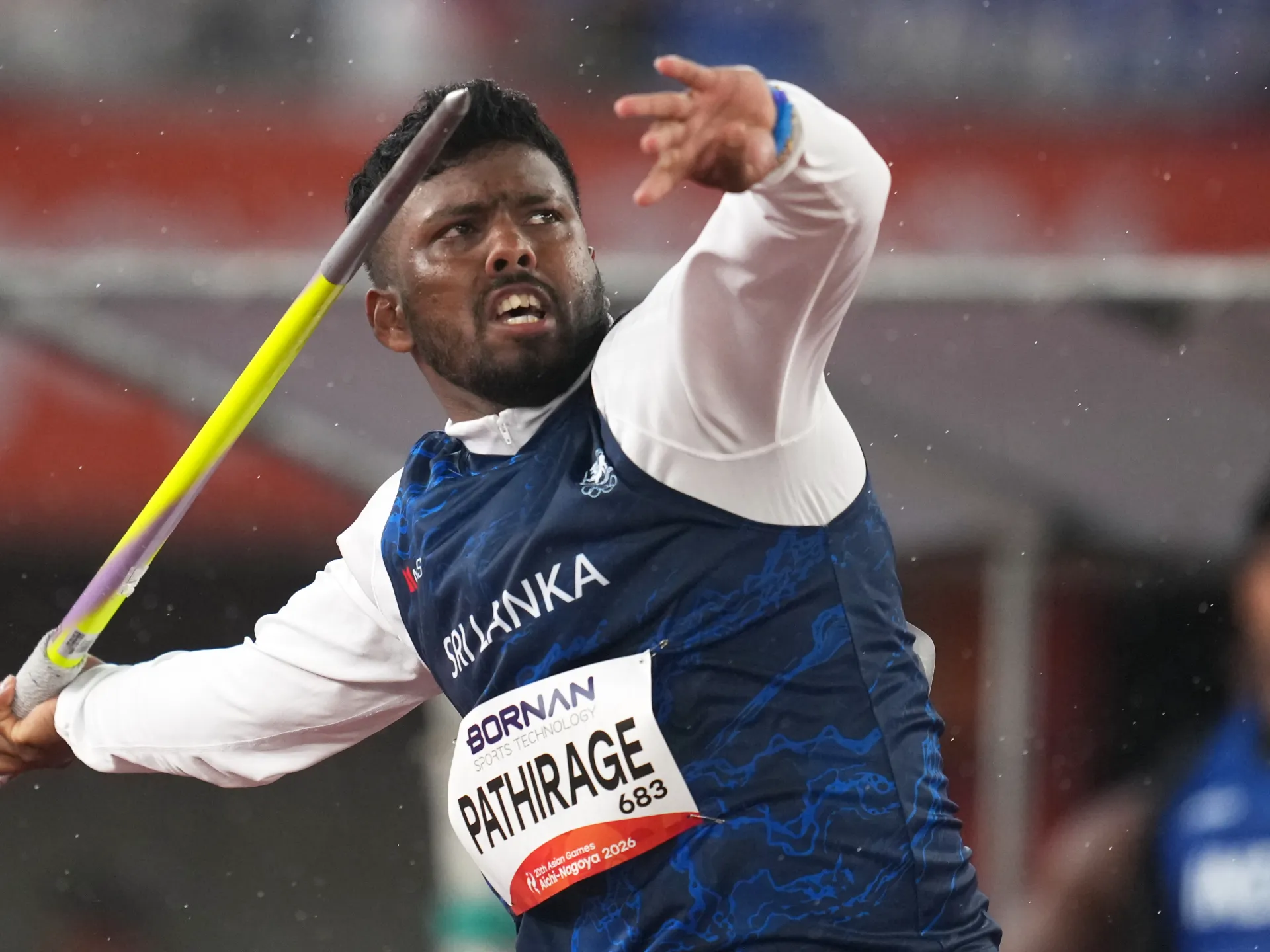 Sri Lankan athlete in a blue uniform throws a javelin, with one arm raised.