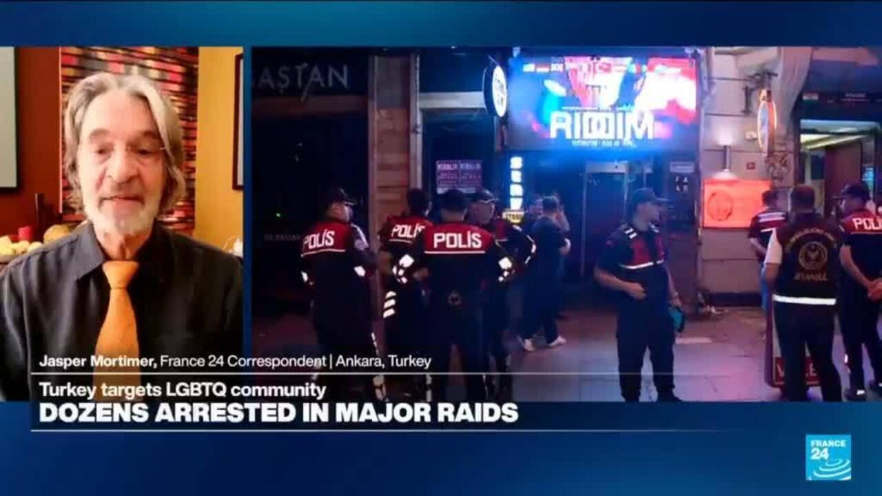 Split-screen news broadcast shows a correspondent beside police officers outside a brightly lit venue.
