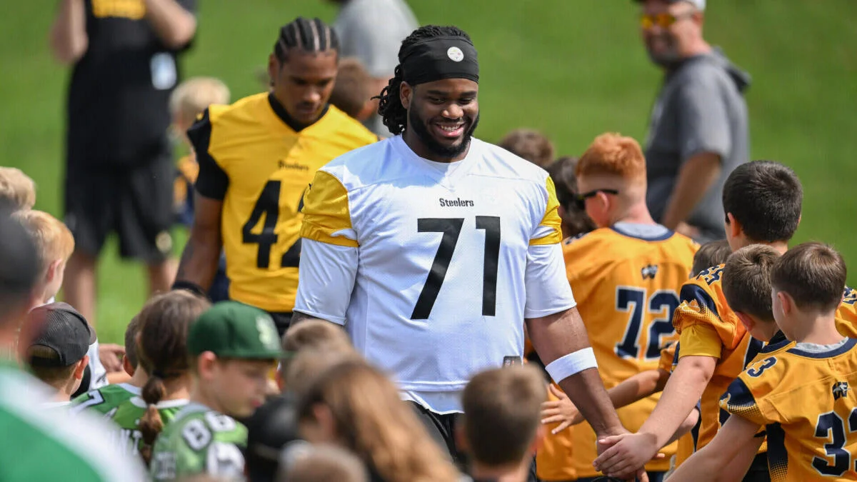 Football player in white Steelers jersey surrounded by youth players at an outdoor event