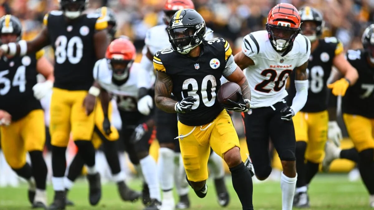 Steelers player number 30 runs with the football as Bengals player number 20 pursues him.