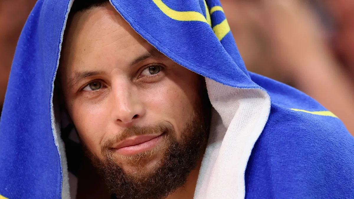 Bearded man draped in a blue and yellow towel looks toward the camera.