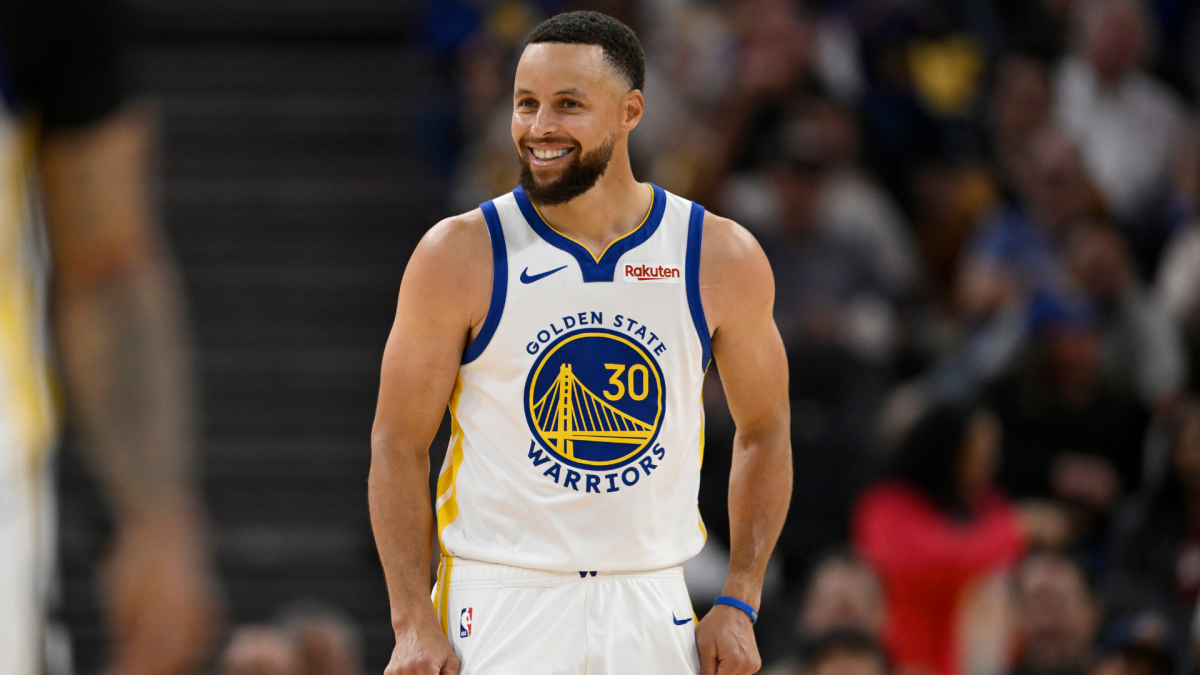 Smiling basketball player in a white Golden State Warriors number 30 uniform stands on the court.