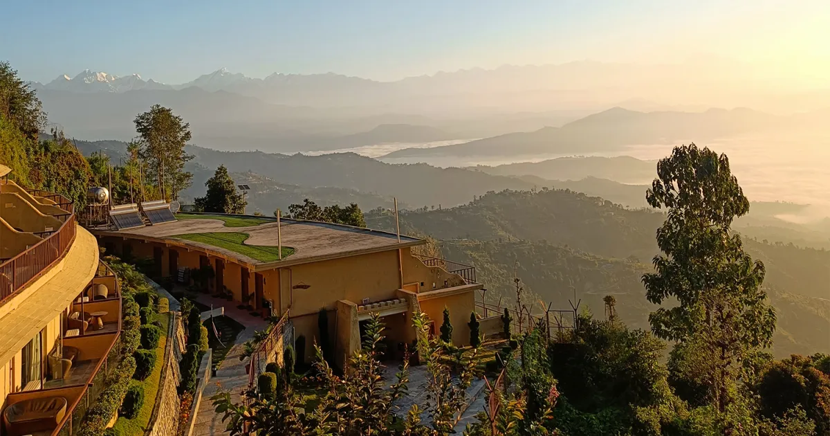 Mountain resort buildings overlook layered, misty hills beneath a warm sunrise.