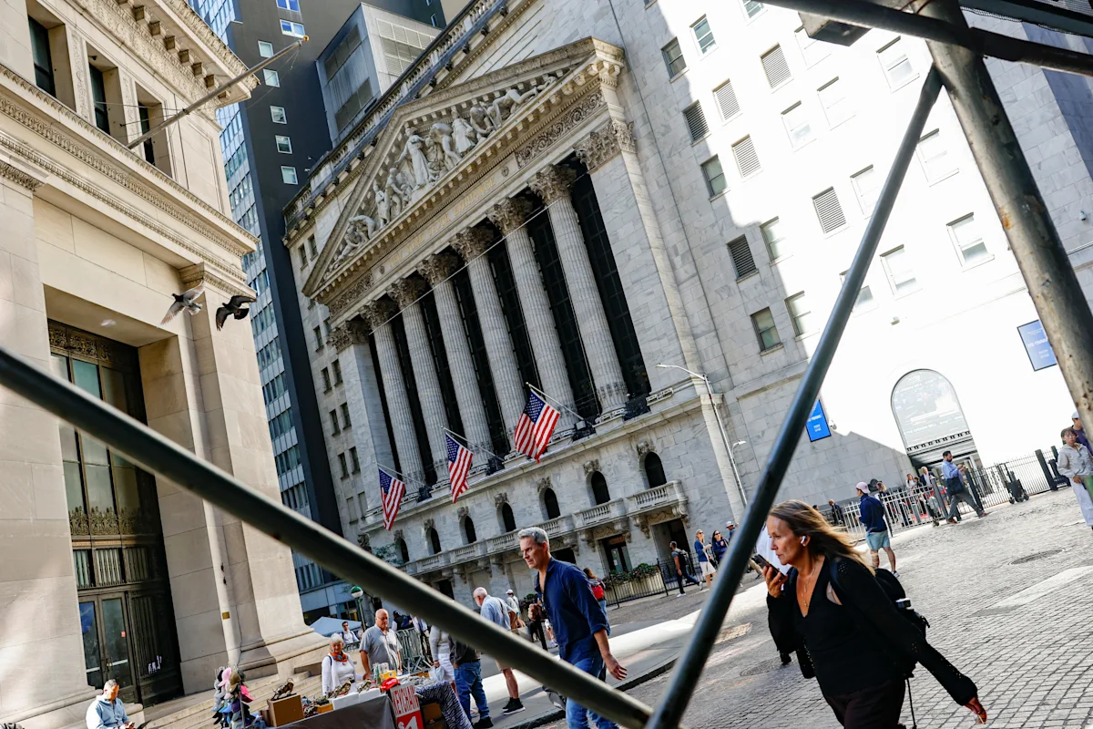 New York Stock Exchange facade with American flags, pedestrians, and scaffolding in foreground