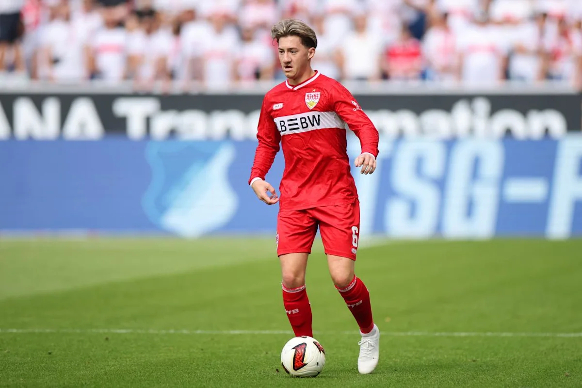 Footballer in red Stuttgart kit dribbles a ball across the pitch during a match
