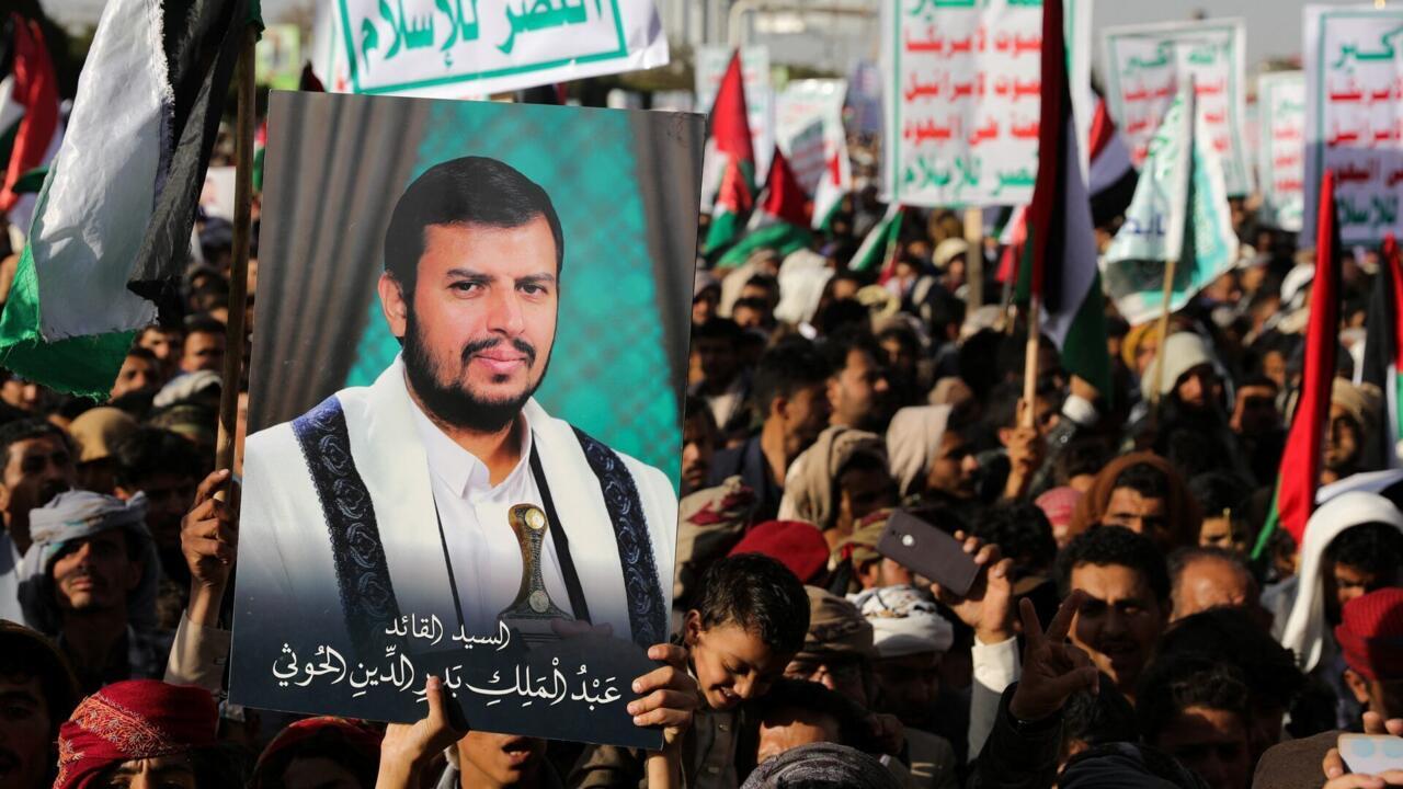 Crowd holds a large portrait and political signs during a public gathering