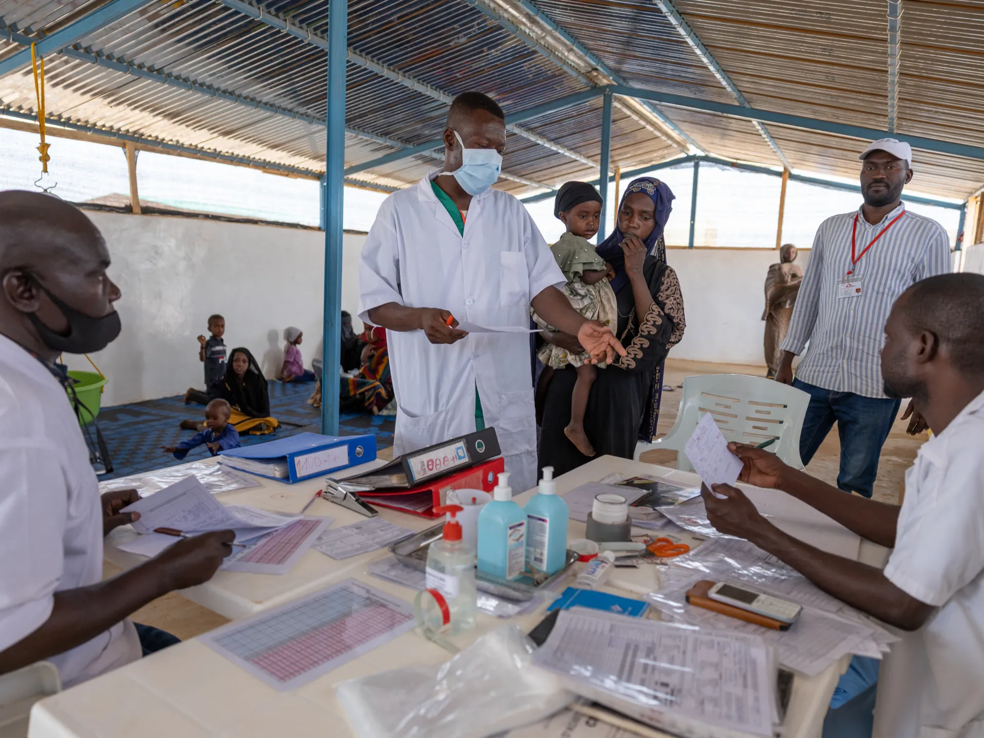 Healthcare workers process patients at a temporary clinic as a mother holds her child.