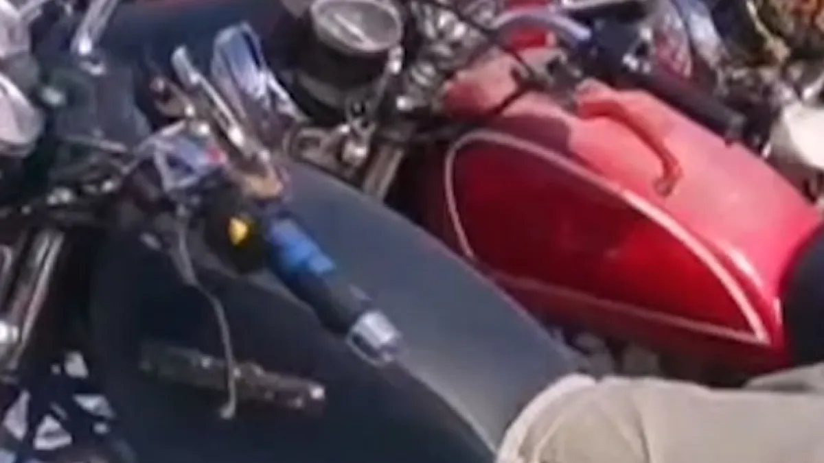 Close view of a red motorcycle beside dark motorcycle parts and a beige-clad person.