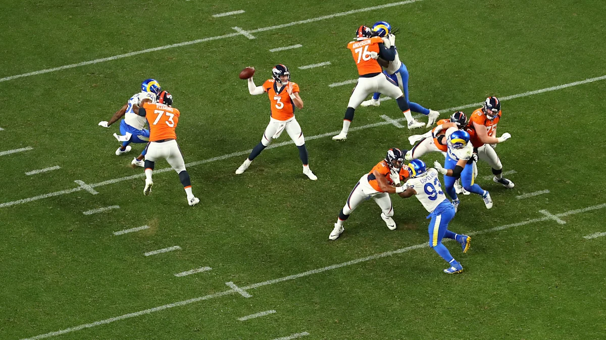 Broncos quarterback throws the football as Rams defenders and blockers engage across the field.