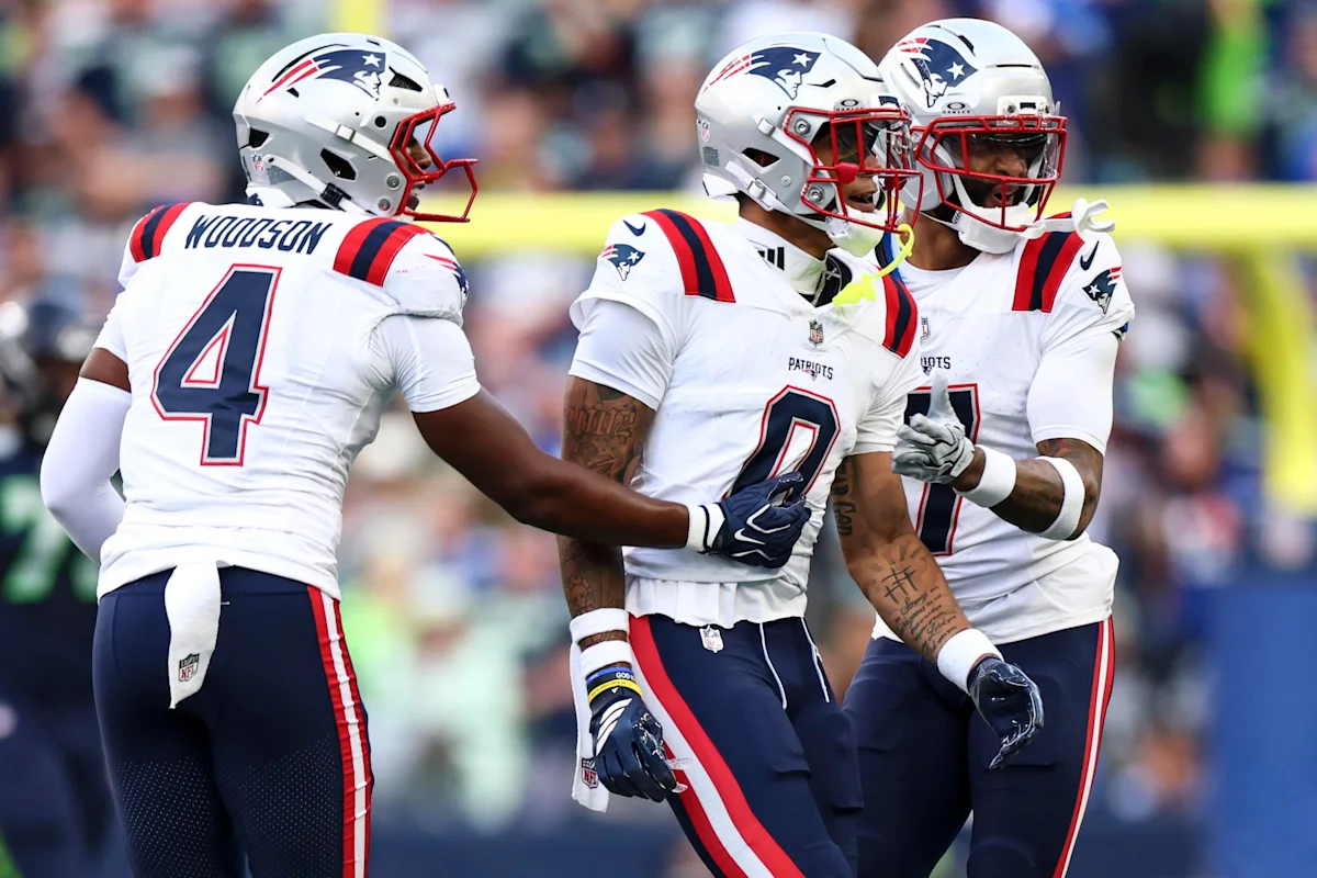 Three New England Patriots players in white uniforms and helmets gather on the field during a game.