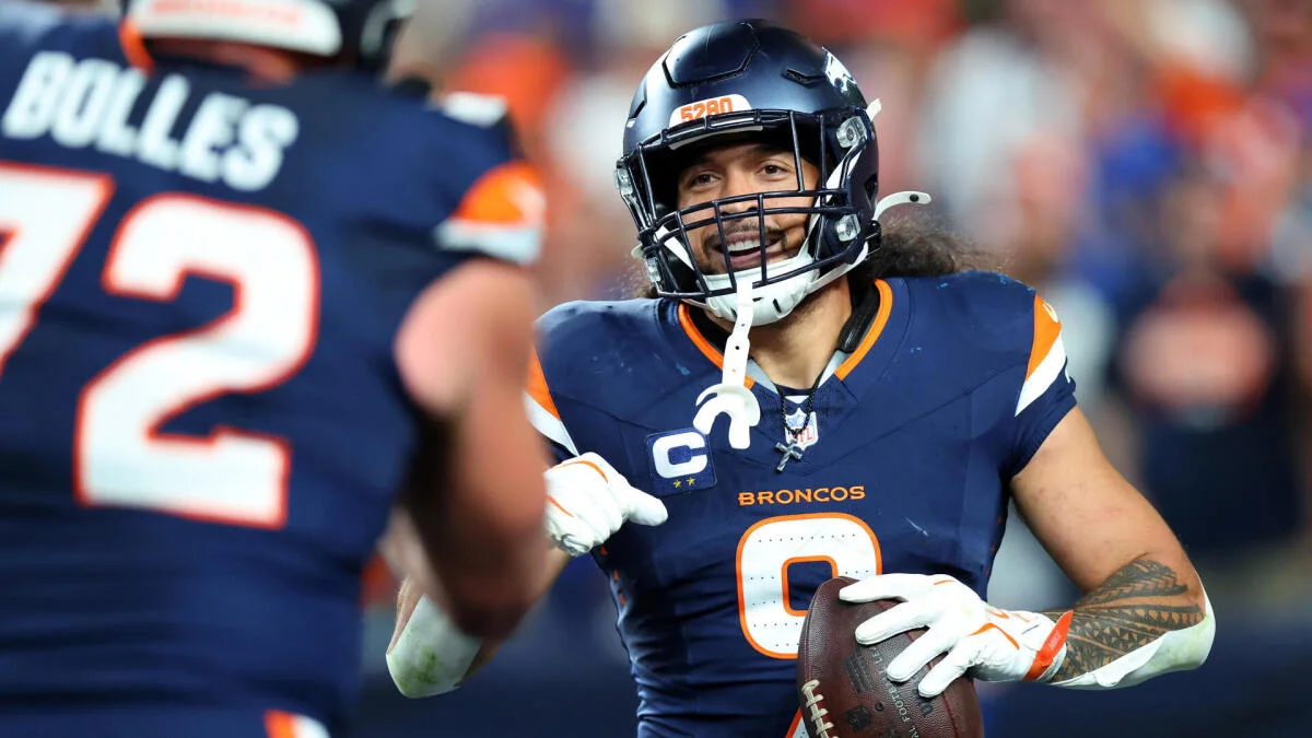 A Denver Broncos player in a navy uniform holds a football beside a teammate wearing number 72.