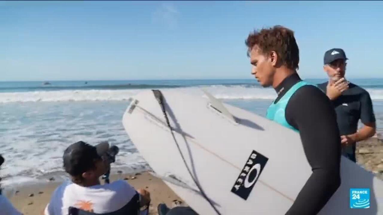 Surfer carrying a white board along the beach as waves break behind him.