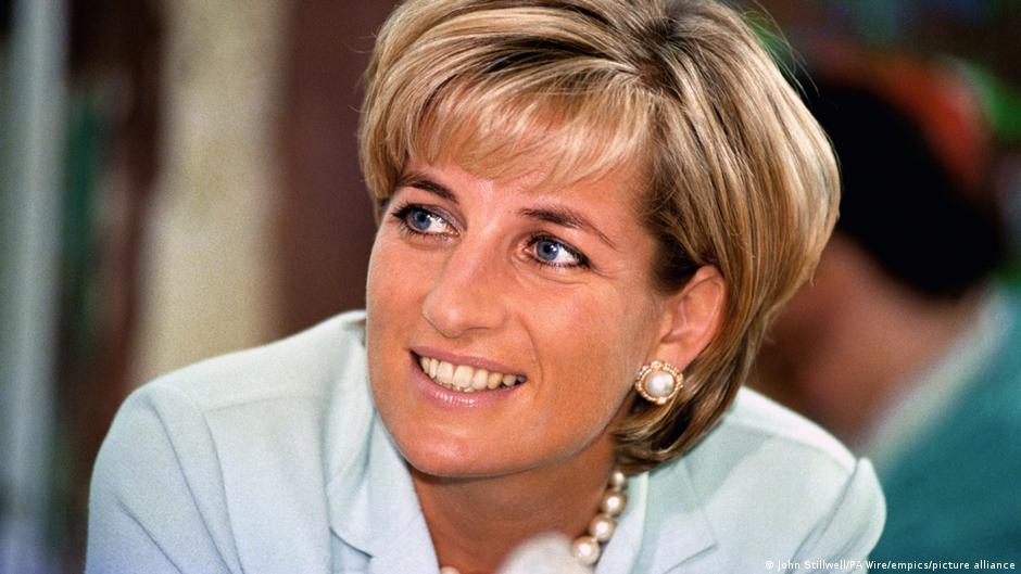 Princess Diana smiling and looking aside while wearing a pale blue jacket and pearl jewelry