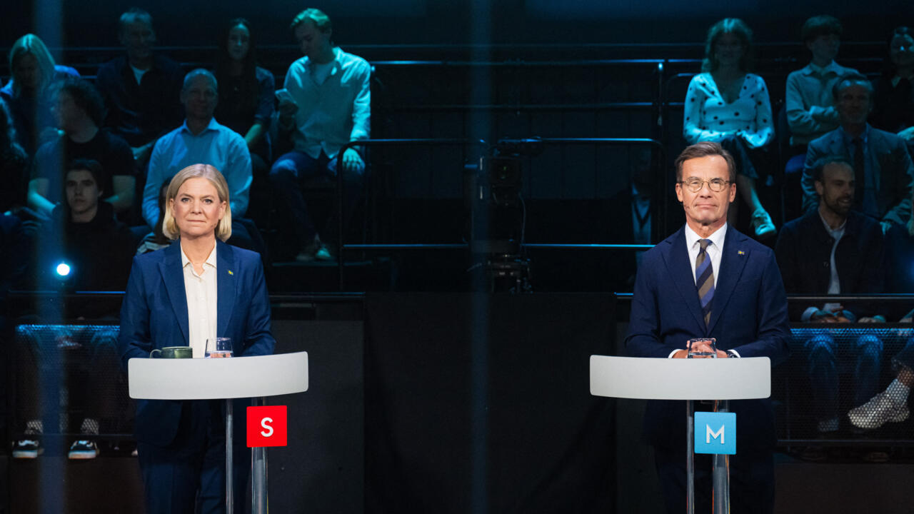 Two political candidates stand at separate podiums during a televised debate before an audience.