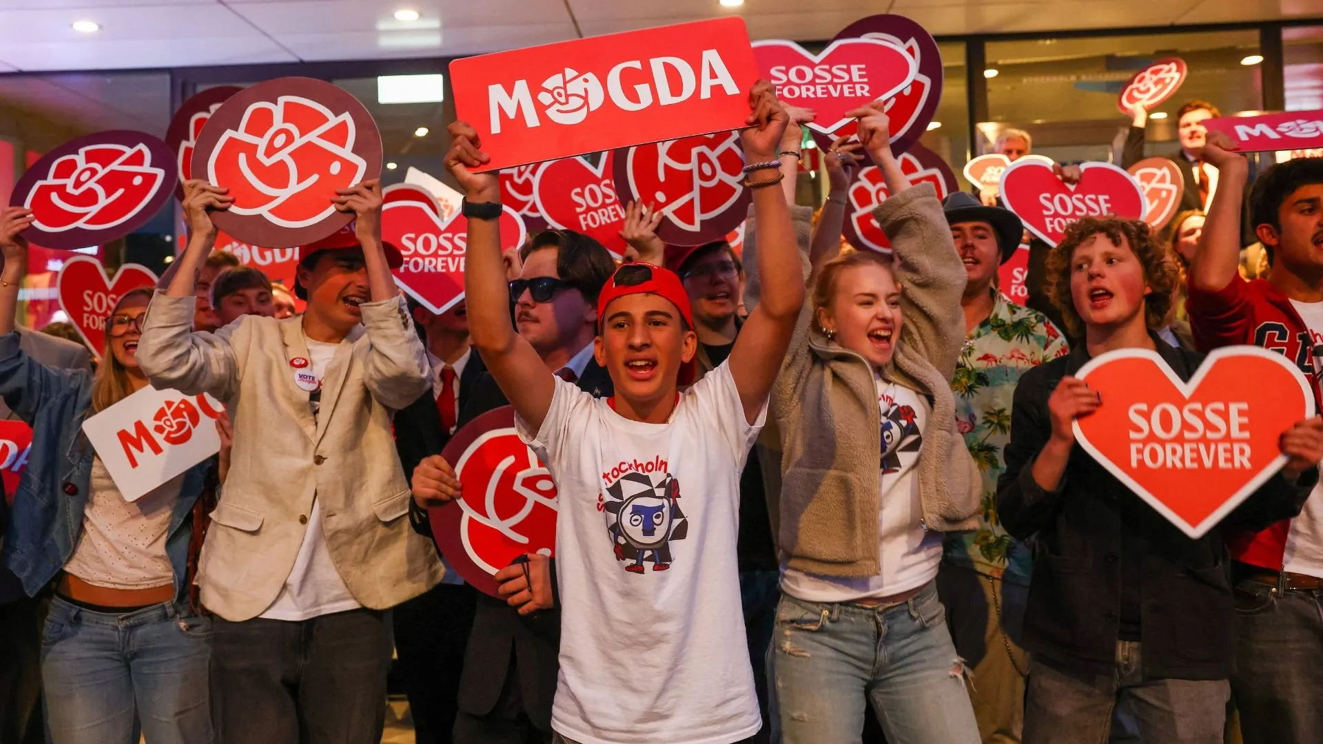 Crowd raises red political signs and heart-shaped placards during a campaign gathering.