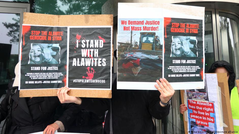 People hold posters reading “Stop the Alawite genocide in Syria” and “Stand with Alawites.”