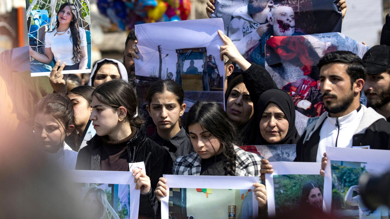 Mourners hold photographs and posters during a crowded outdoor demonstration.
