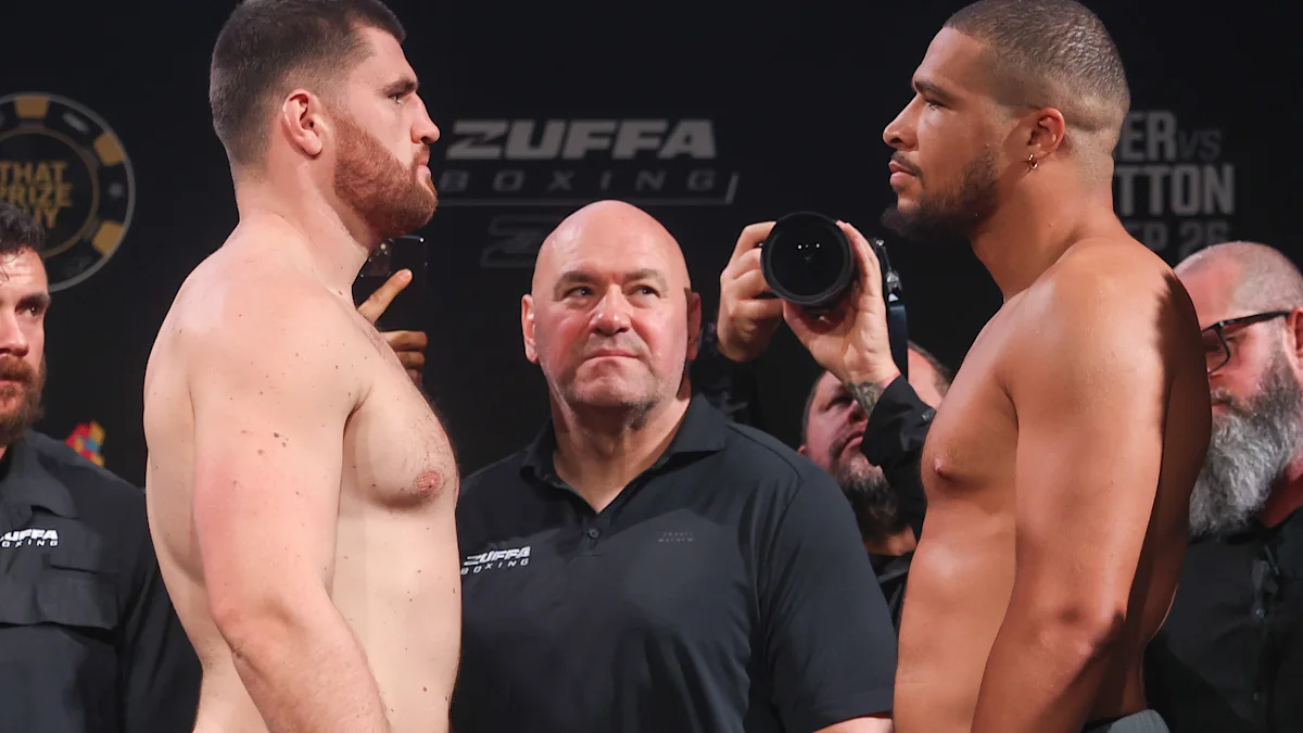 Two shirtless fighters face each other at a weigh-in as an official stands between them.