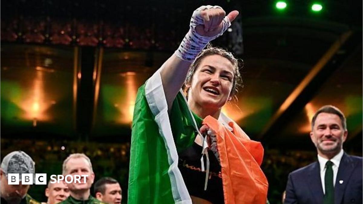 Smiling female boxer raises her bandaged fist while draped in Irish colours inside an arena
