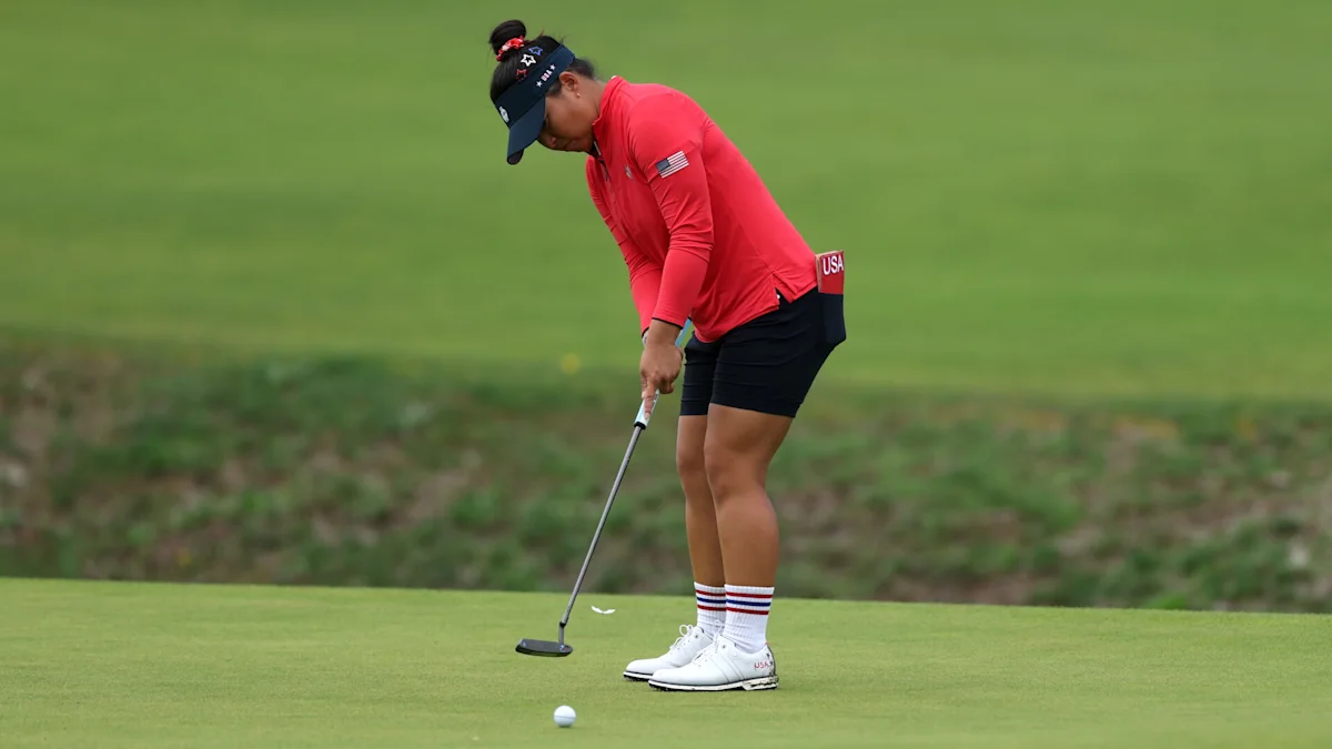 Golfer in red shirt and black shorts lining up a putt on a green