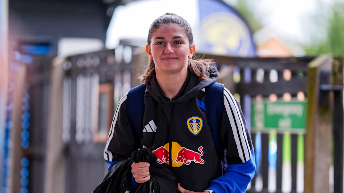 Footballer wearing a Leeds United training jacket and backpack, standing outdoors and looking at camera
