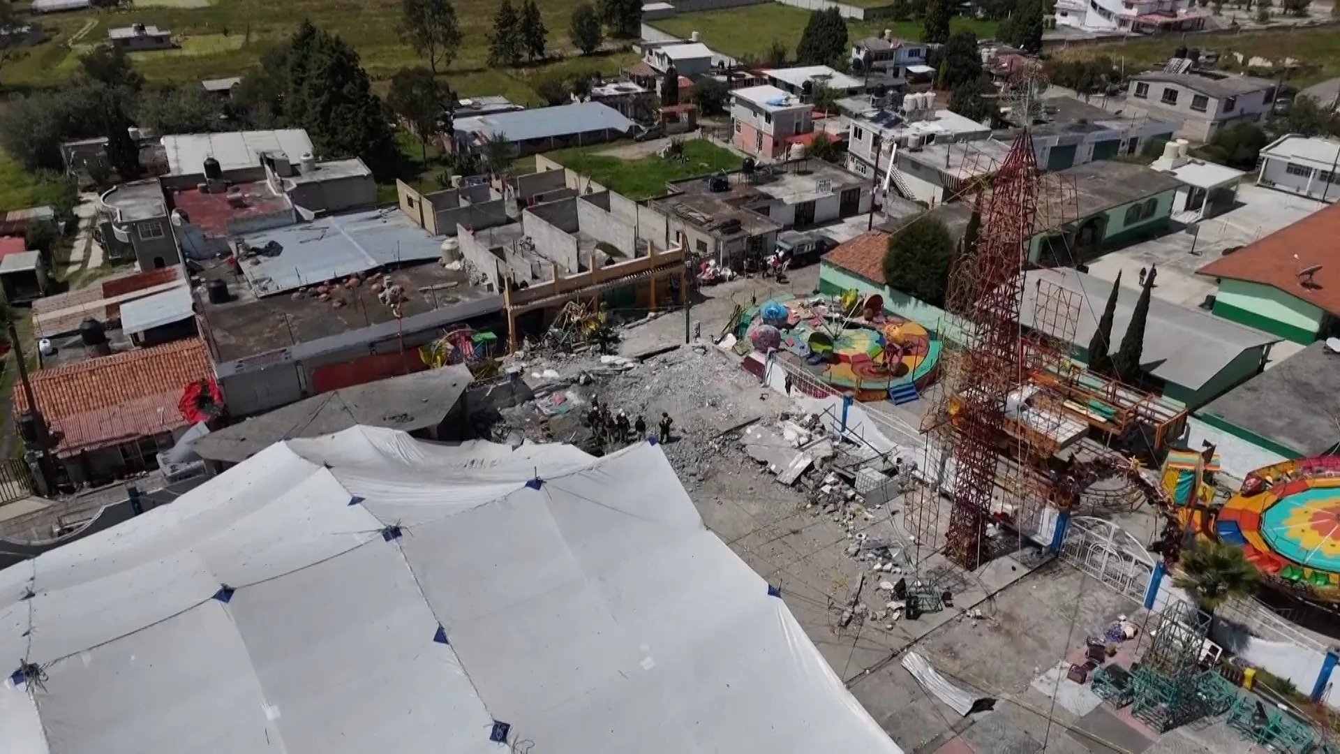 Aerial view of rubble, damaged buildings, tents and colorful amusement rides in a neighborhood.