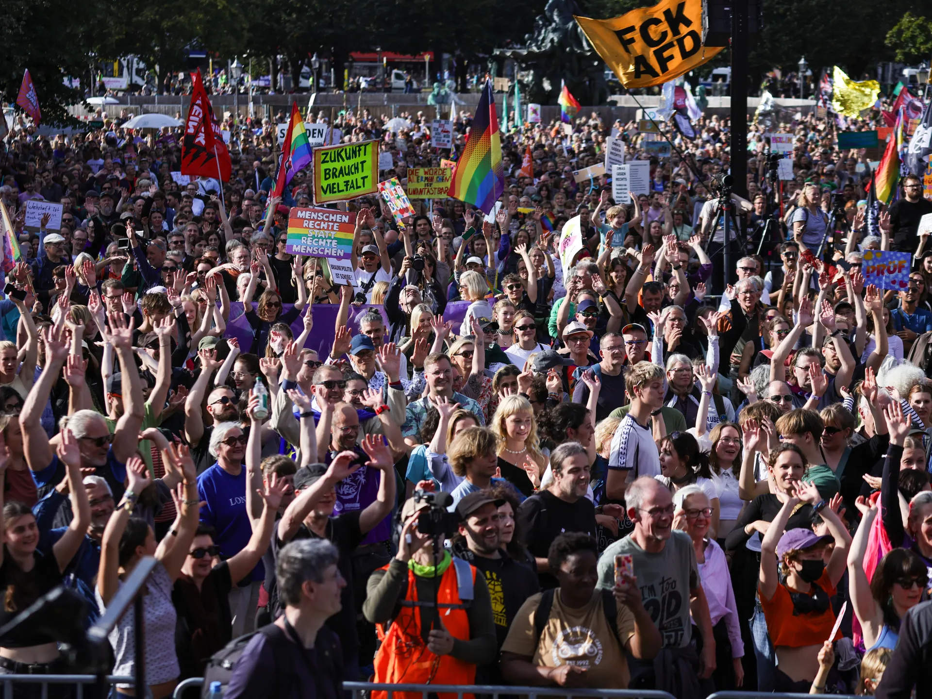 Large crowd waving hands and rainbow flags at a demonstration with anti-AfD signs