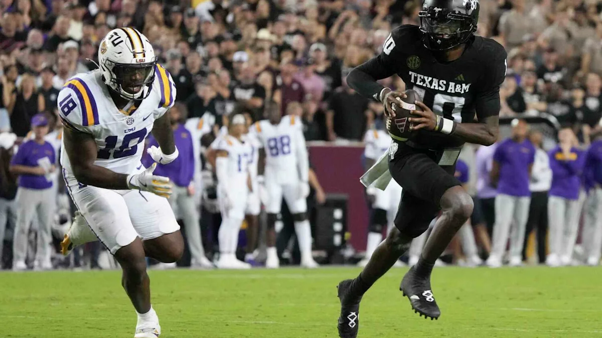A Texas A&M player runs with the football as an LSU player pursues on the field.