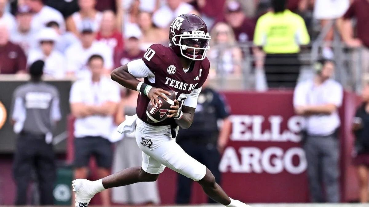 Texas A&M football player in maroon jersey runs with the ball during a game.