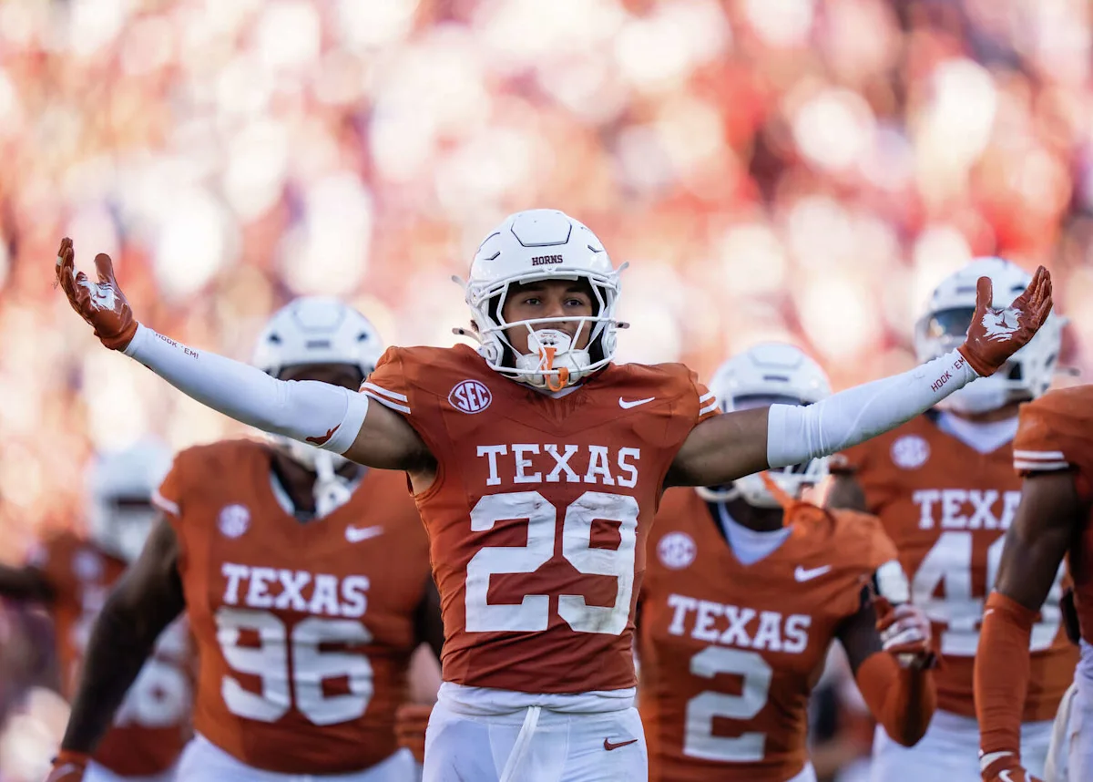 Texas football player wearing number 23 raises his arms as teammates stand behind him.