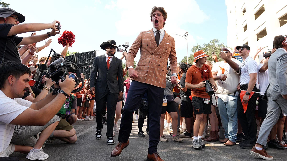 Young man in a plaid suit walks through a crowd of photographers and spectators.