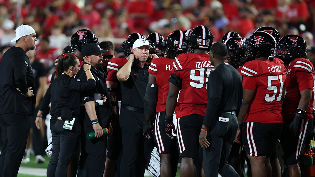 Texas Tech football players and coaches gather in a sideline huddle during a game.