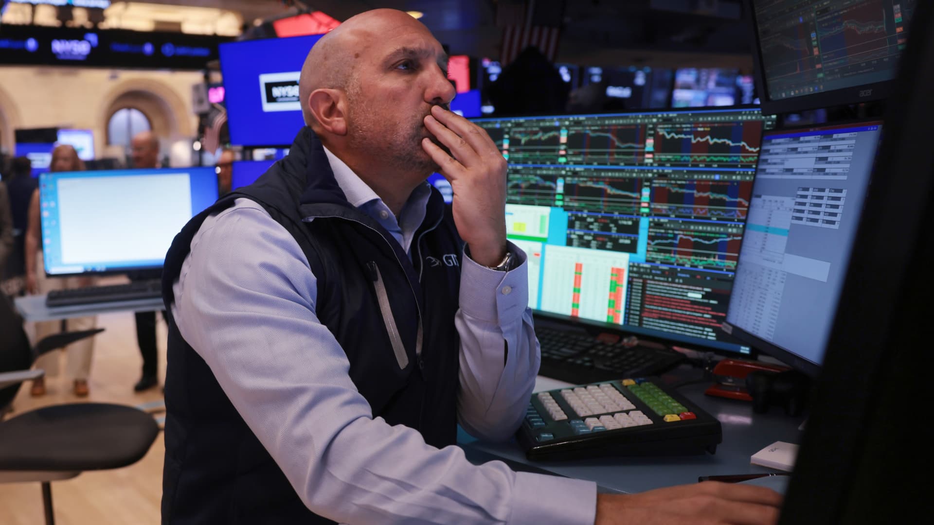 Trader watches financial market screens while seated at a trading desk.