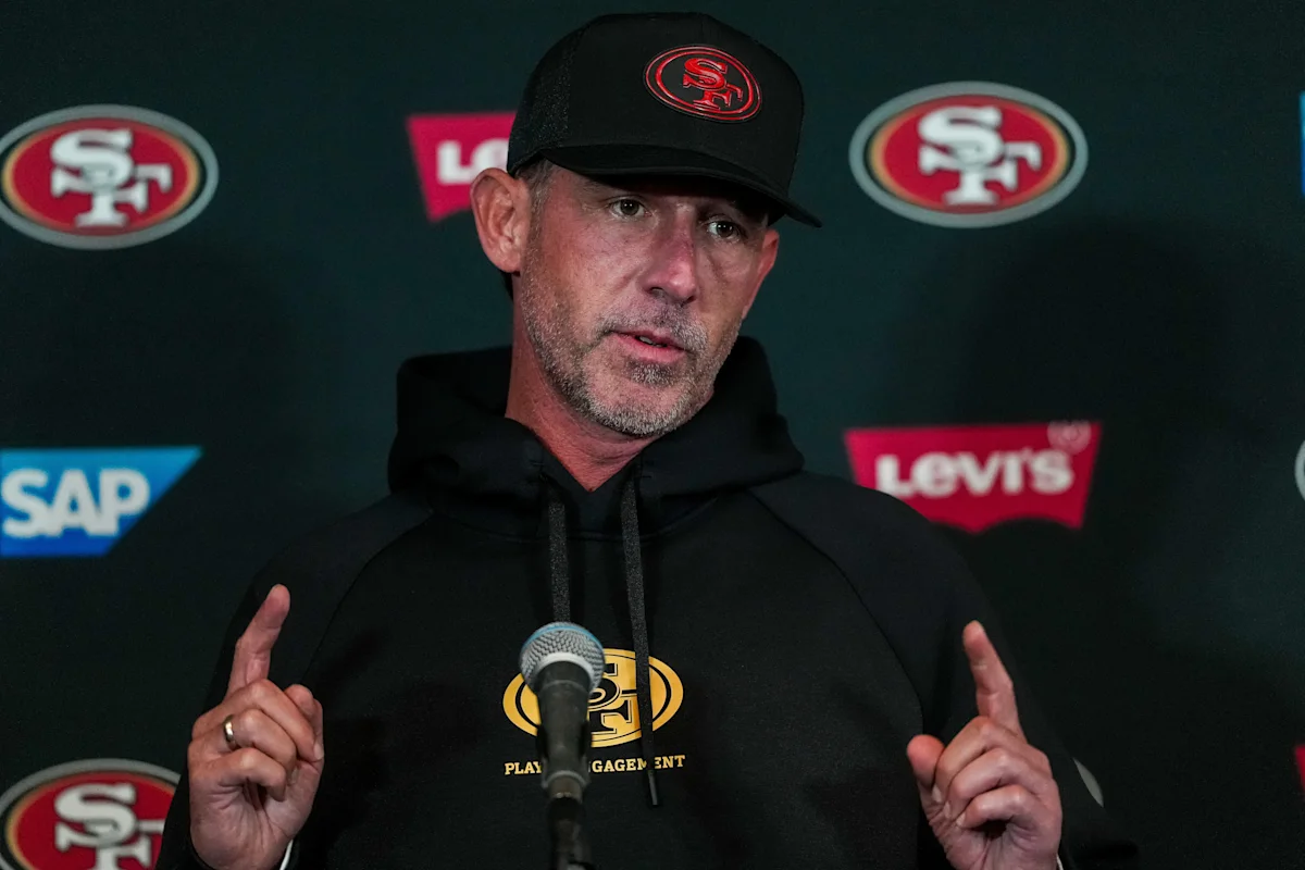 Man in San Francisco 49ers cap and hoodie speaks at a press conference