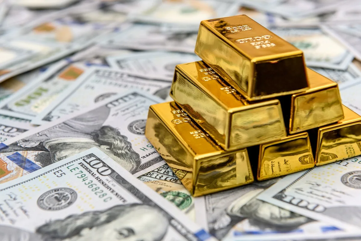 Stacked gold bars resting on a spread of U.S. dollar banknotes