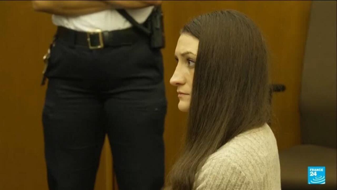 Woman with long brown hair sits in profile inside a courtroom.