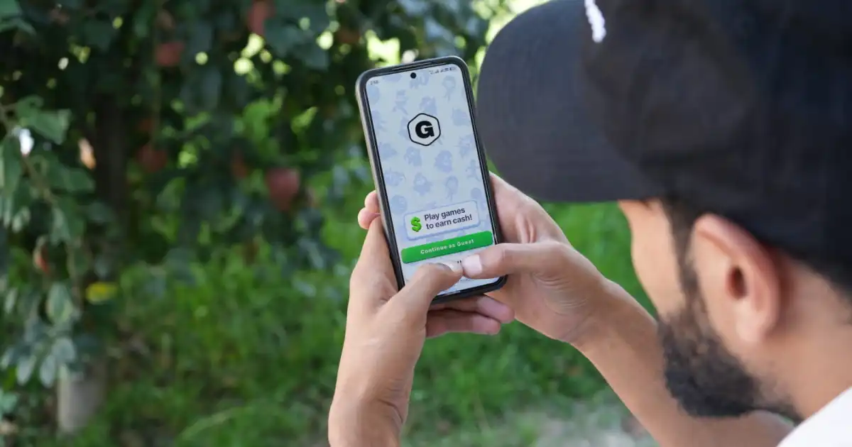 Person holding a smartphone displaying a game advertisement promising cash rewards outdoors