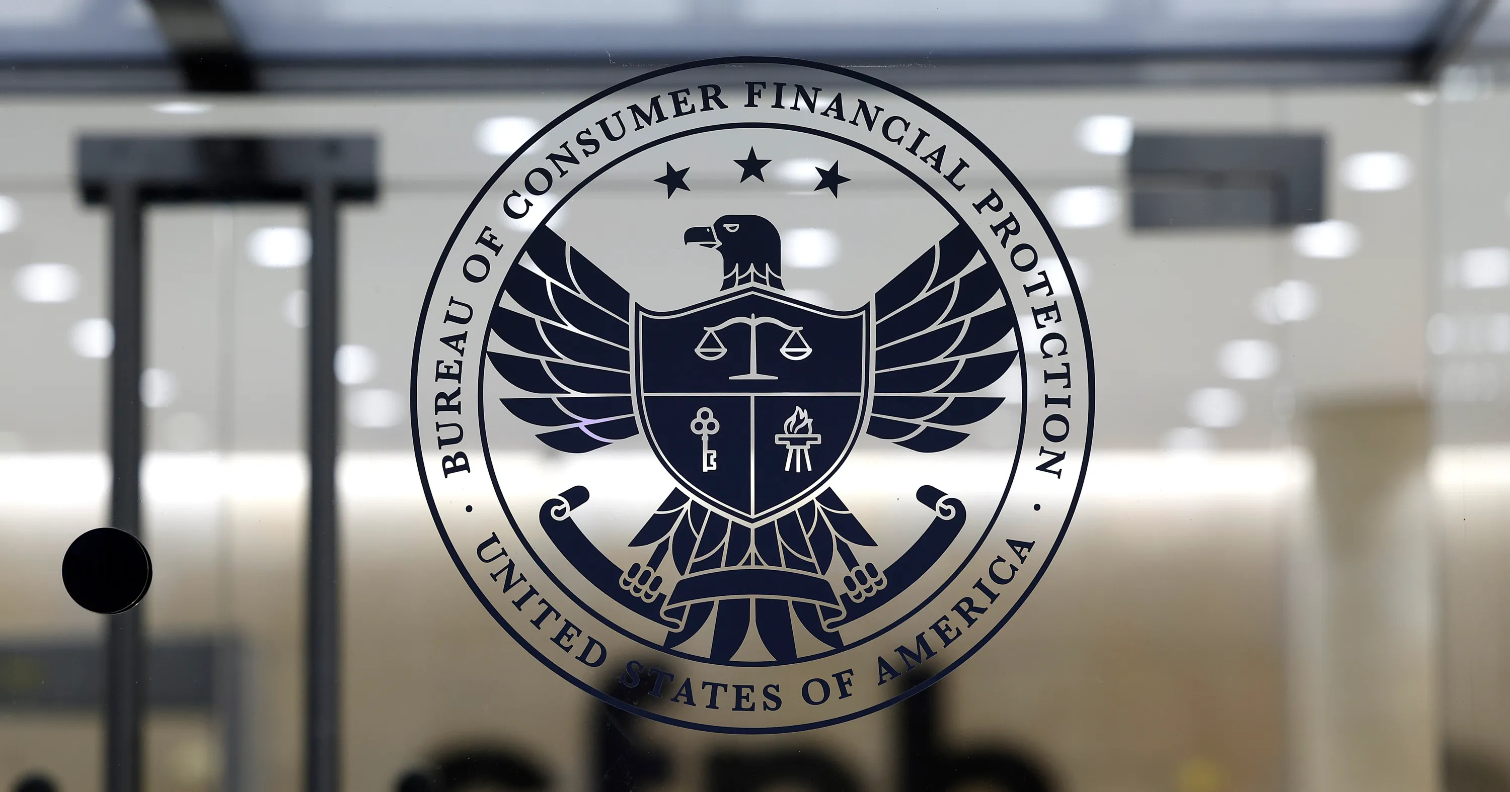 Large Bureau of Consumer Financial Protection seal displayed over a blurred office interior.