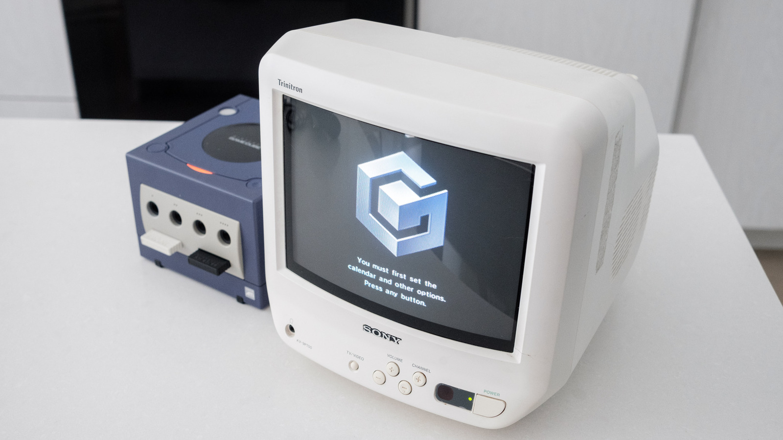 Nintendo GameCube console sits beside a white Sony Trinitron television displaying the GameCube logo.