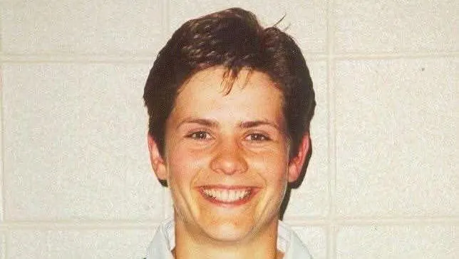 A smiling young person with short dark hair wearing a light collared shirt.