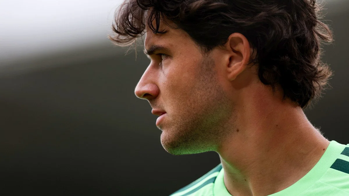 Close-up side profile of a dark-haired footballer wearing a bright green sports jersey