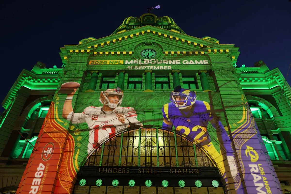 Green-lit historic station facade displaying projected NFL players and Melbourne game promotional text at night