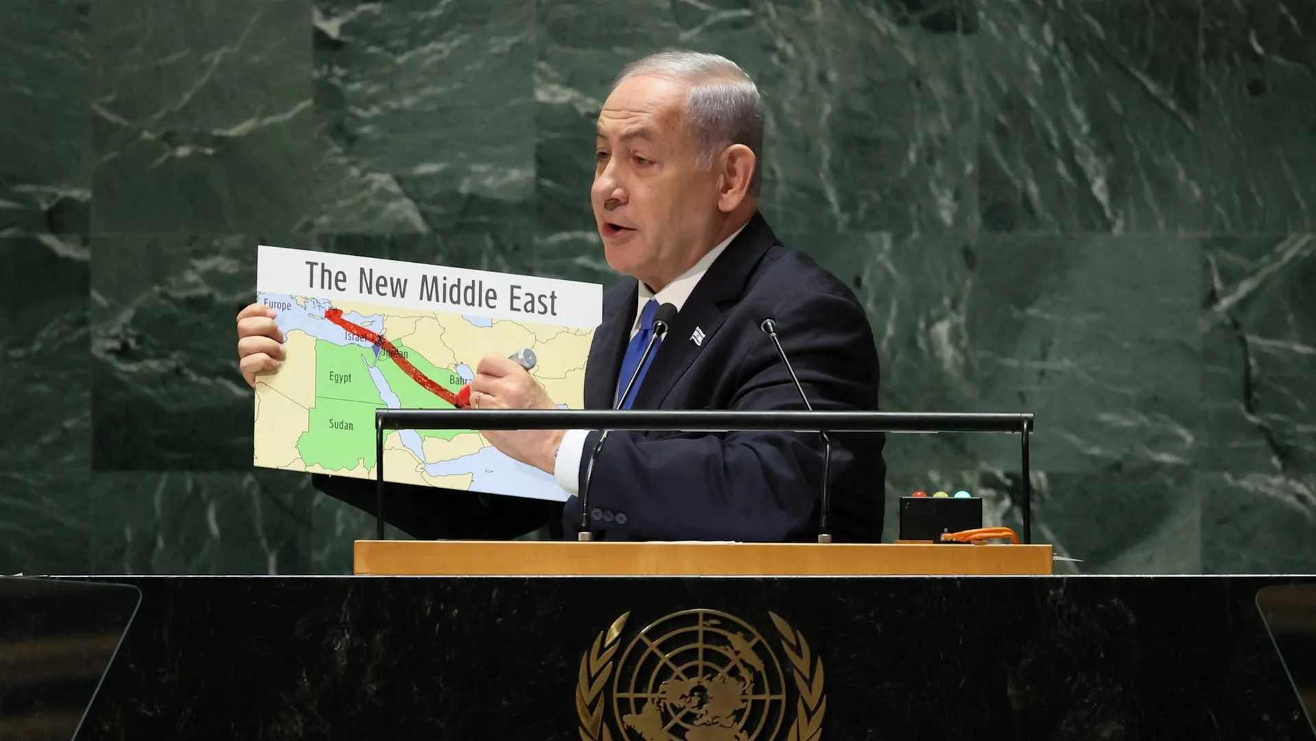 A suited speaker holds a “The New Middle East” map at a UN podium.