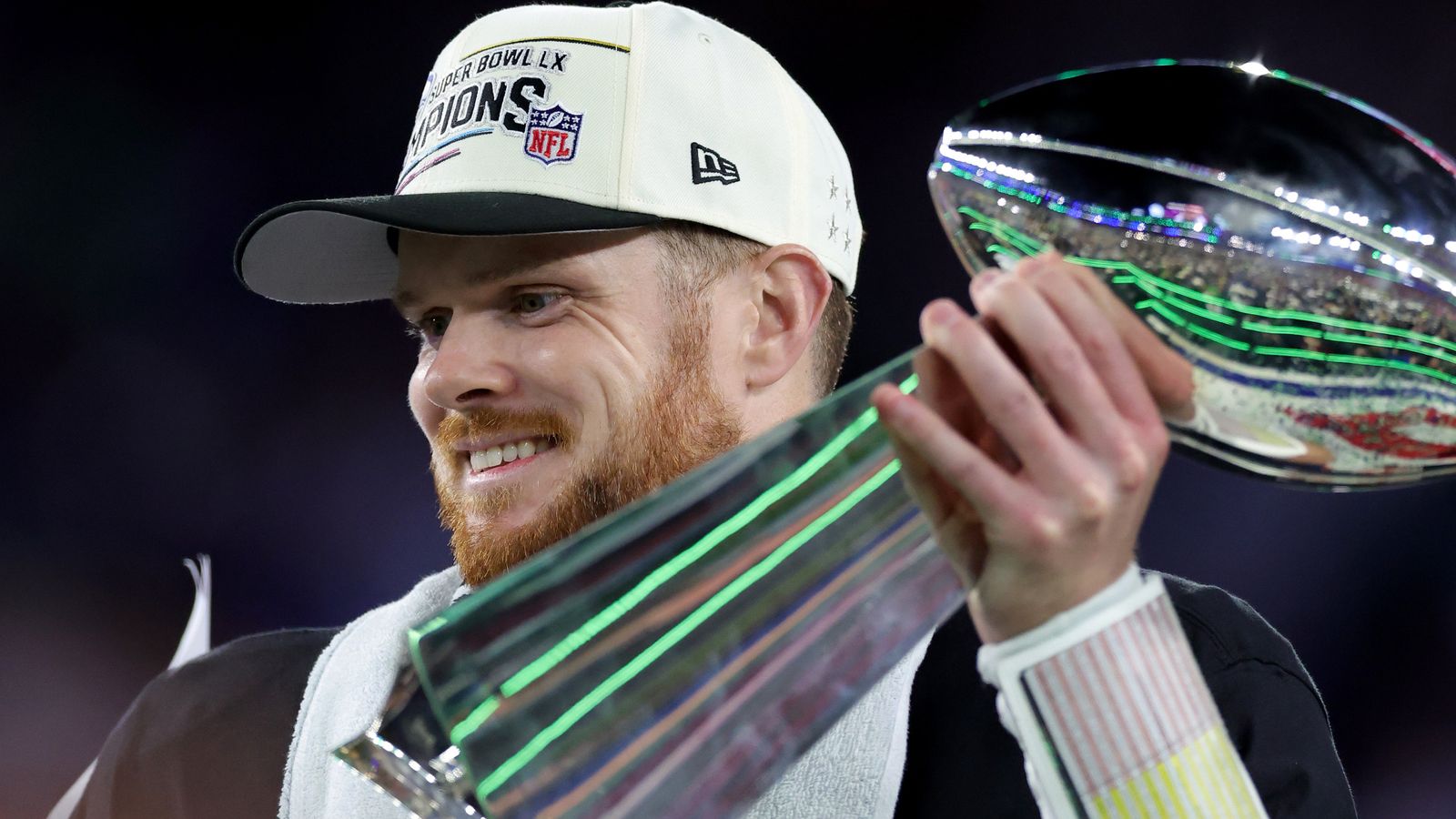 Football player in championship cap smiles while holding the Lombardi Trophy aloft